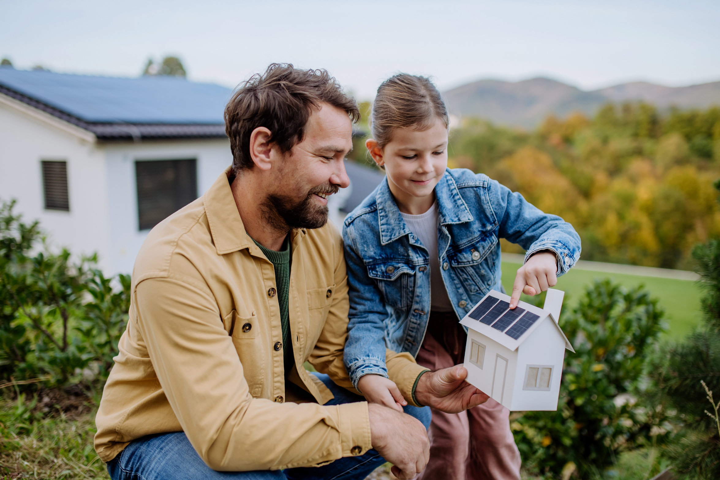 Father and daughter with a model house with solar panels in a garden