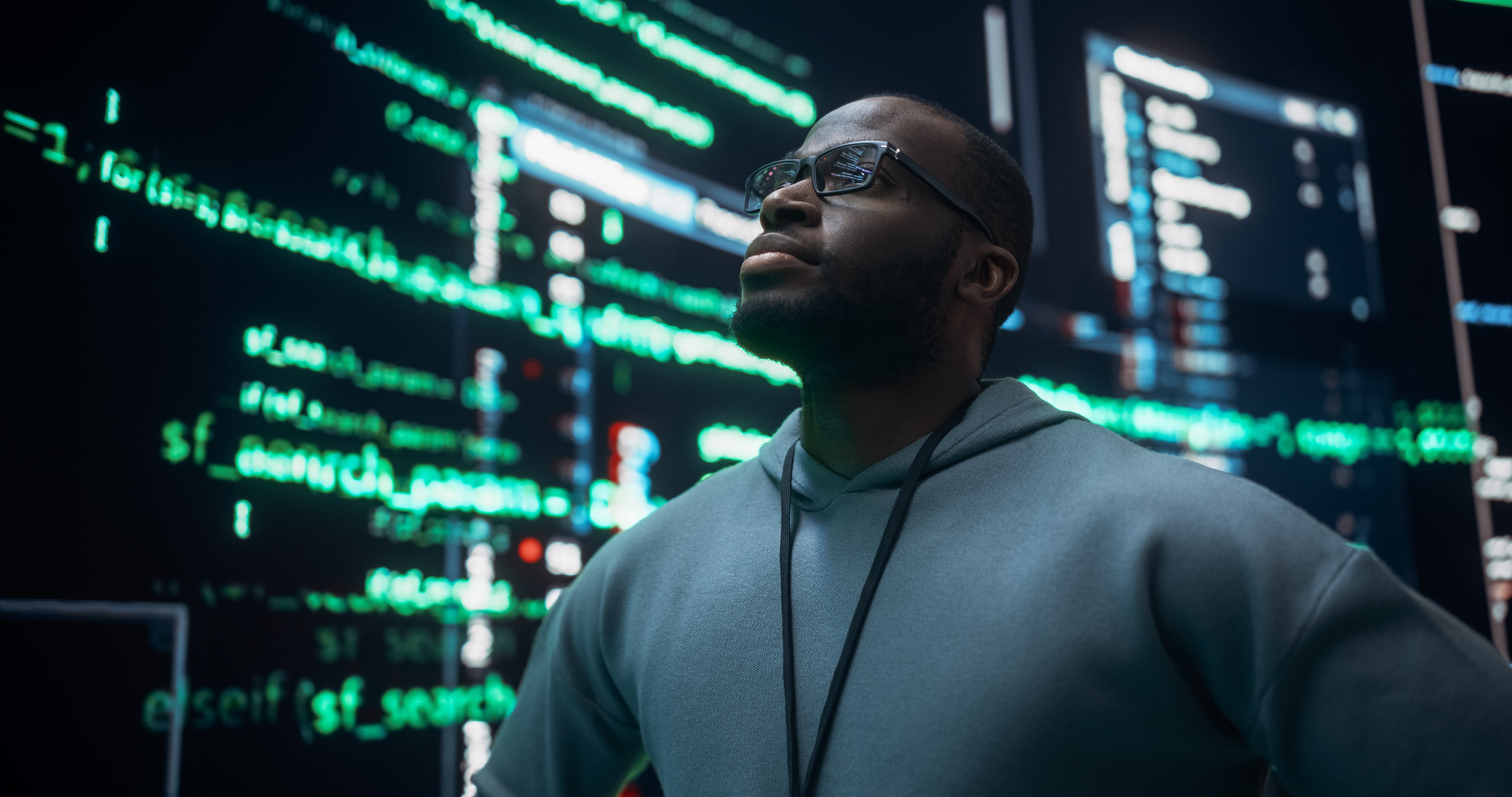 Confident professional looking upward in front of large illuminated code screens